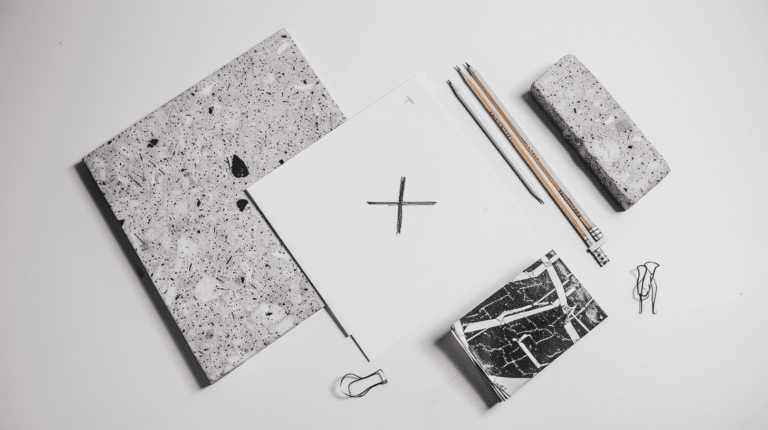 Feuilles de travail et crayons posés sur une surface blanche, avec un X tracé au crayon symbolisant la refonte d'une identité de marque